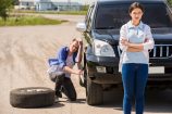 Young man changing the punctured tyre on his car.